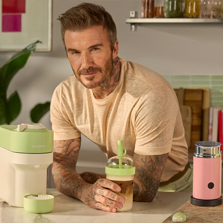 David Beckham holding a tumbler with Pistachio Vanilla Over Ice coffee smiling into the distance.